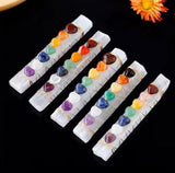 A collection of chakra wands, each with a handle and decorated with various colorful crystals representing the chakras, set against a dark background.