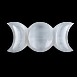 A top-down studio shot of a white satin spar dish carved into a triple moon symbol.