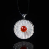 A white mineral necklace with a round pendant featuring a white flower pattern with a red center.