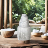 A handmade gypsum tower LED lamp with a wooden stand. Placed on a table in a room with natural background.