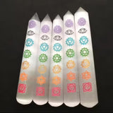 Five polished white wands engraved with the seven colorful chakra symbols against a black background.