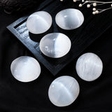 A collection of polished white palm stones displayed on a dark surface. 
