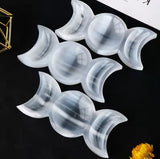 Three polished white gypsum triple moon trays are arranged diagonally on a dark surface.